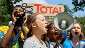 Greta Thunberg auf einer Demonstration gegen Total mit anderen Aktivist*innen. Sie Schreit in ein Megafon.